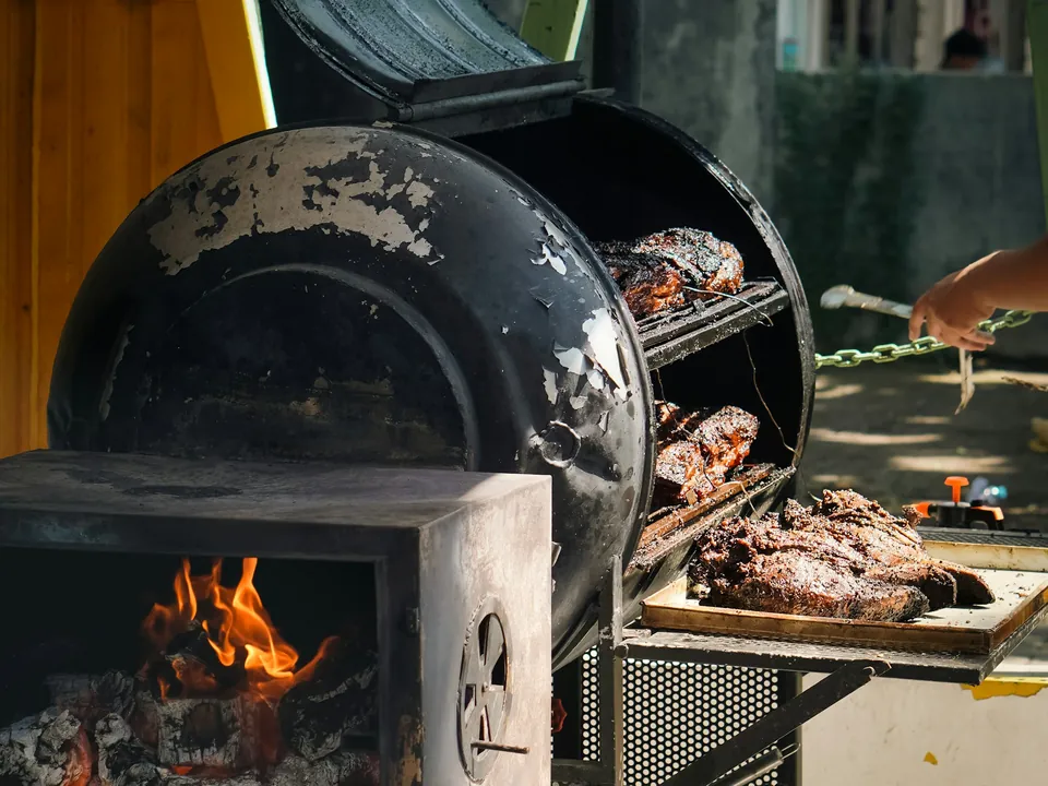 An offset smoker running low and slow, with a wood fire in the firebox and meat on the racks