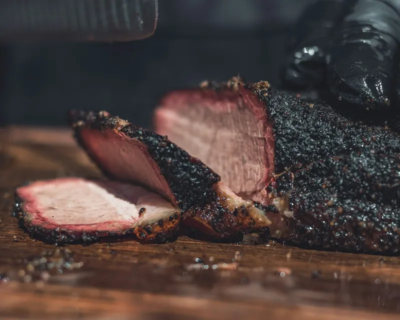 Sliced smoked brisket with a dark pepper bark on a wooden cutting board