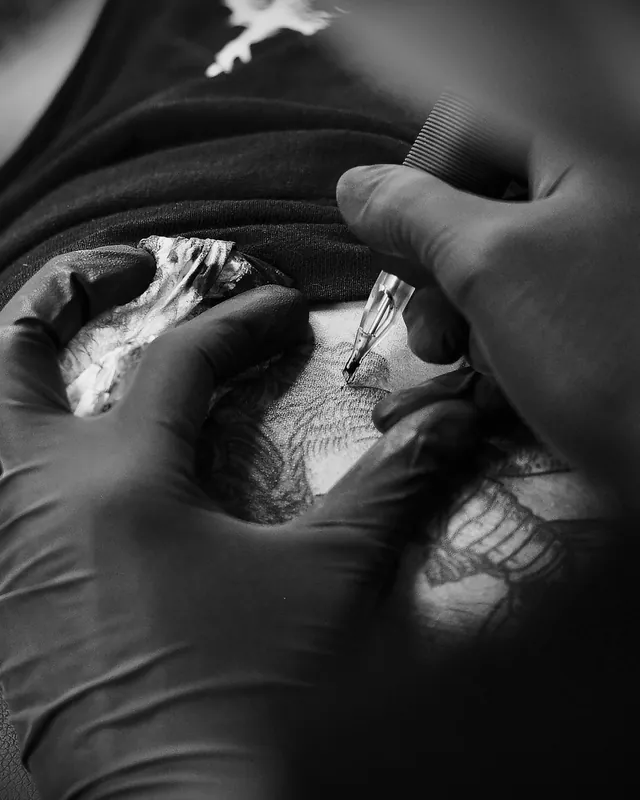 Gloved hands shading a black and grey tattoo, shot in black and white