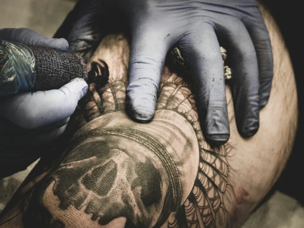 Gloved hands shading a black and grey skull tattoo