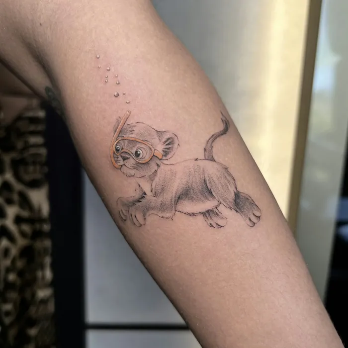 Fine line tattoo of a lion cub in a snorkel mask on a forearm