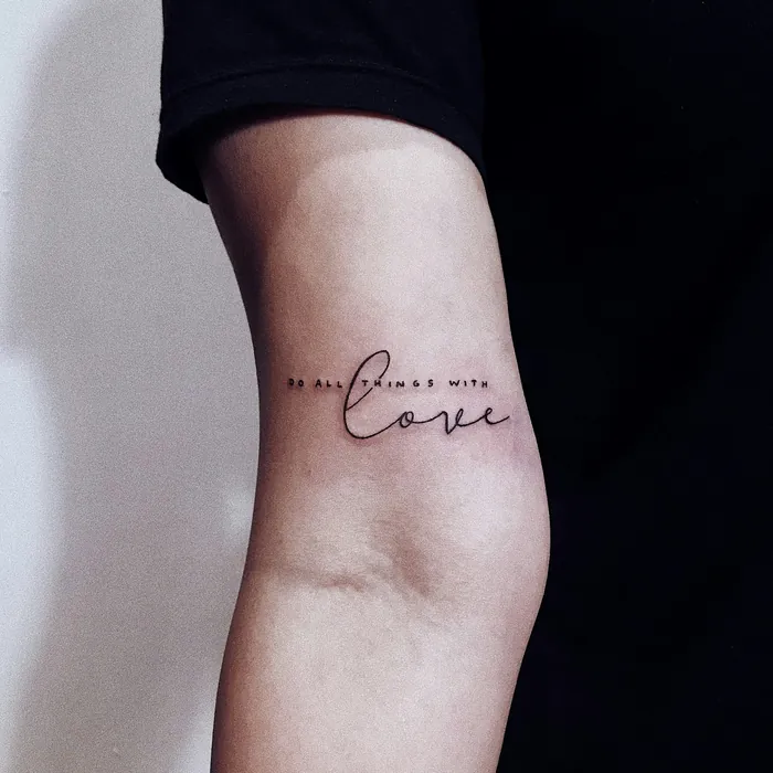 Script lettering tattoo reading do all things with love on an upper arm