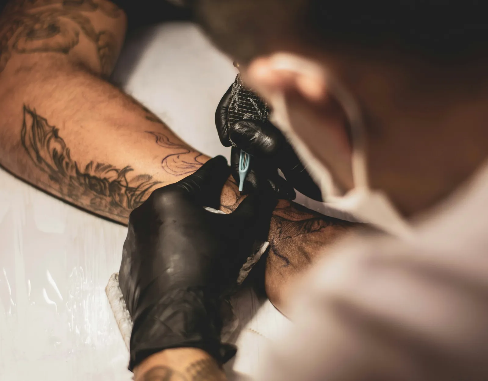 A tattoo artist in black gloves working a black and grey piece on a forearm