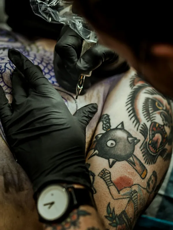 Gloved hands adding to bold traditional style tattoos on a shoulder